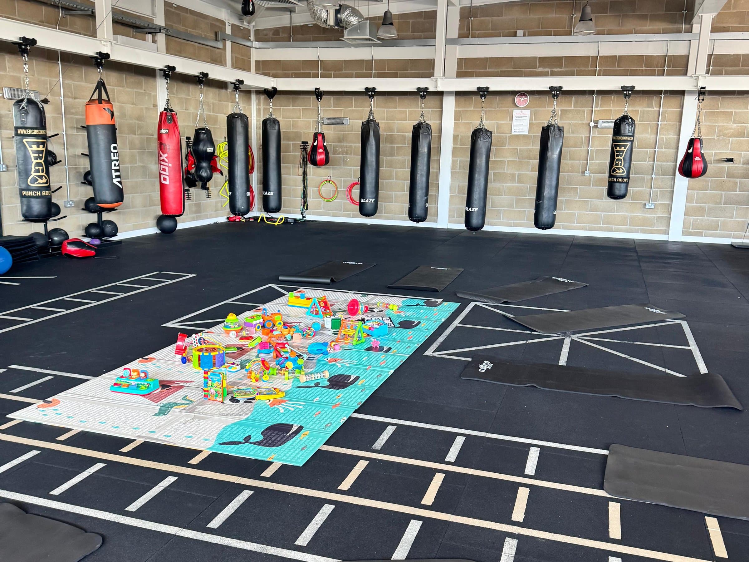 Exercise mats and a play mat of toys set out on the hall floor beneath a row of punchbags