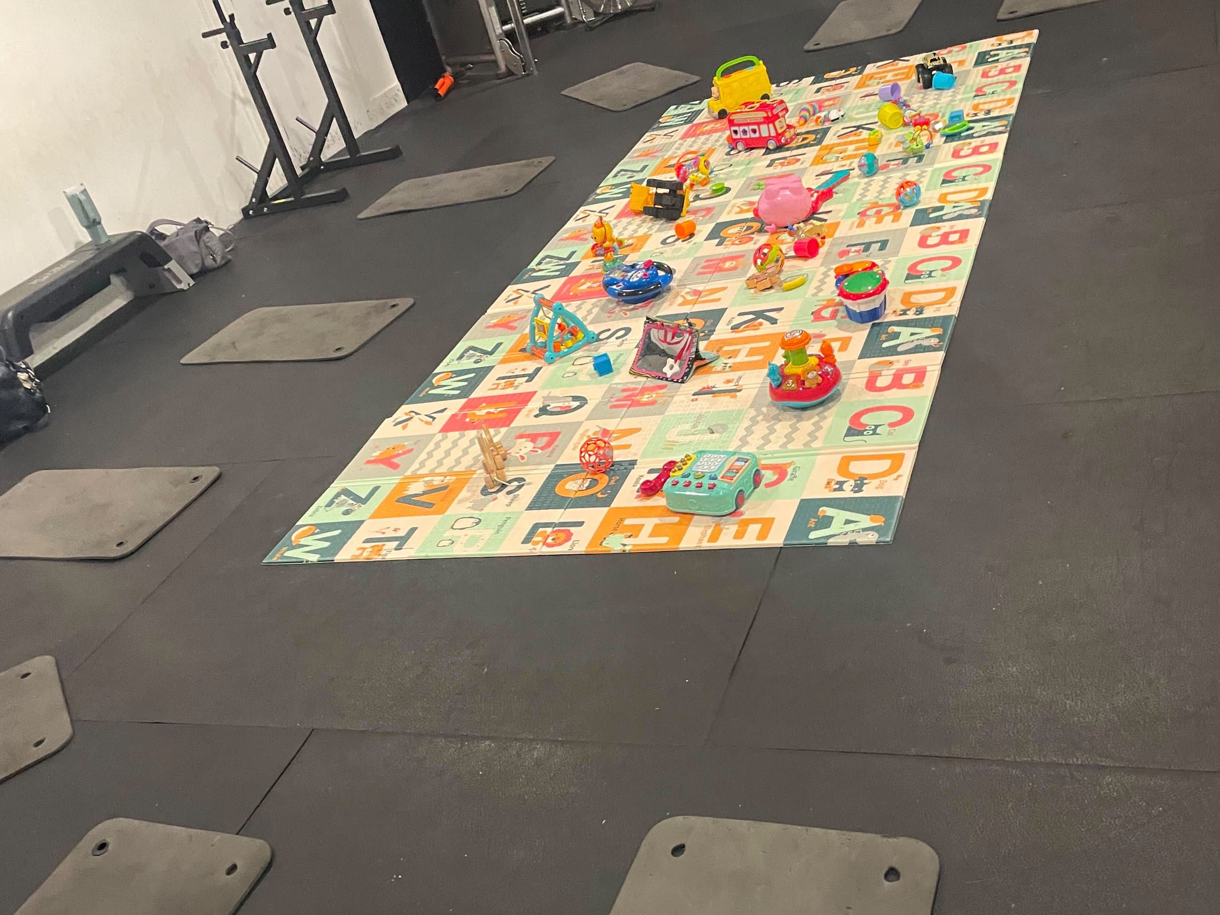 Exercise mats in a ring around an alphabet play mat covered in toys, on the studio floor